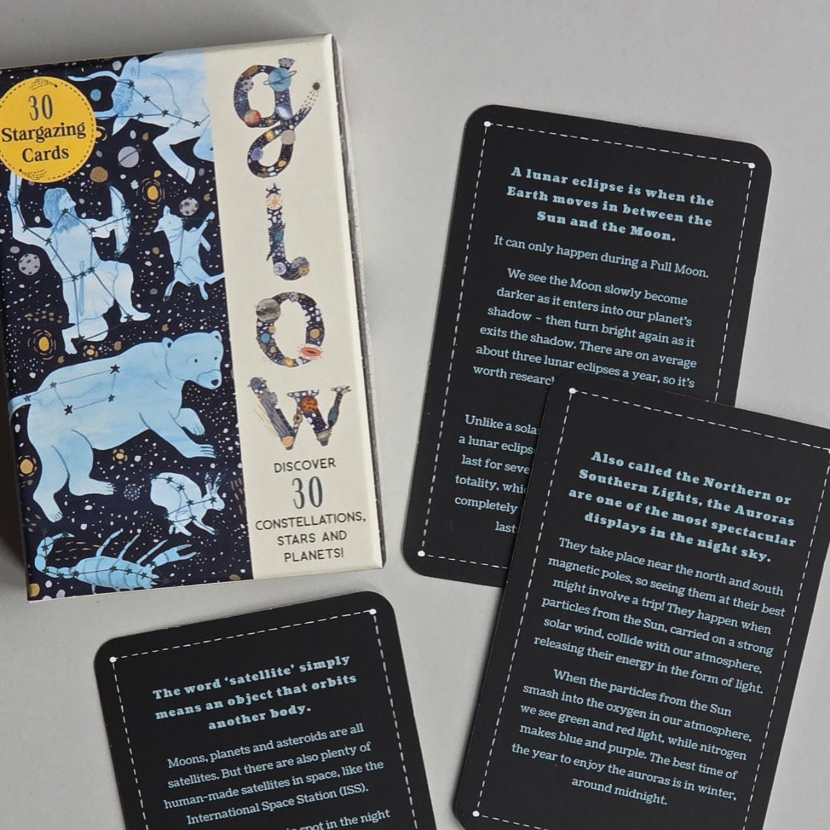 A boxed card deck titled 'Celestial' with illustrated cover art and three black instruction cards laid out on a light grey surface. The packaging and cards explain stargazing constellations and the Moon.