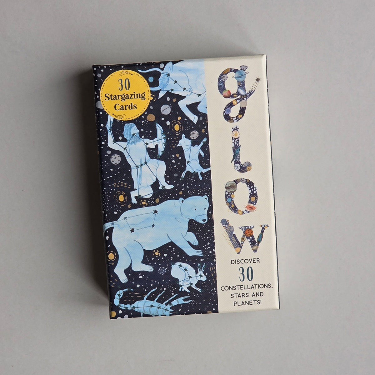 A boxed card deck titled 'Glow' with a dark starry space design, light blue zodiac and animal illustrations, and a yellow circular badge that reads '30 Stargazing Cards' on a plain light grey background.