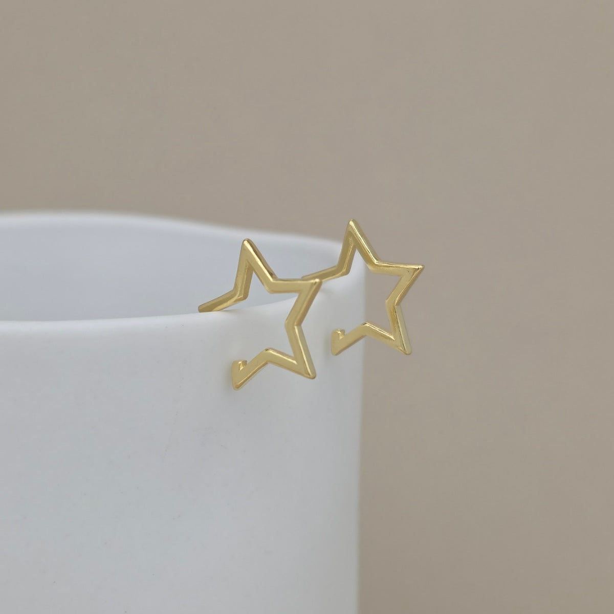 Gold star-shaped earrings on a white surface with a beige background