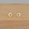 A pair of gold sunburst stud earrings resting on a light brown wooden surface.