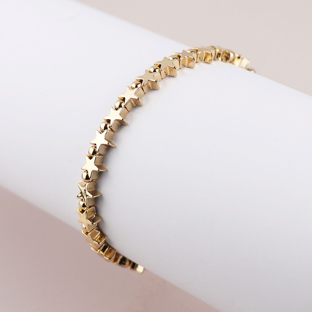 Gold bracelet with star-shaped beads on a white and pink gradient background