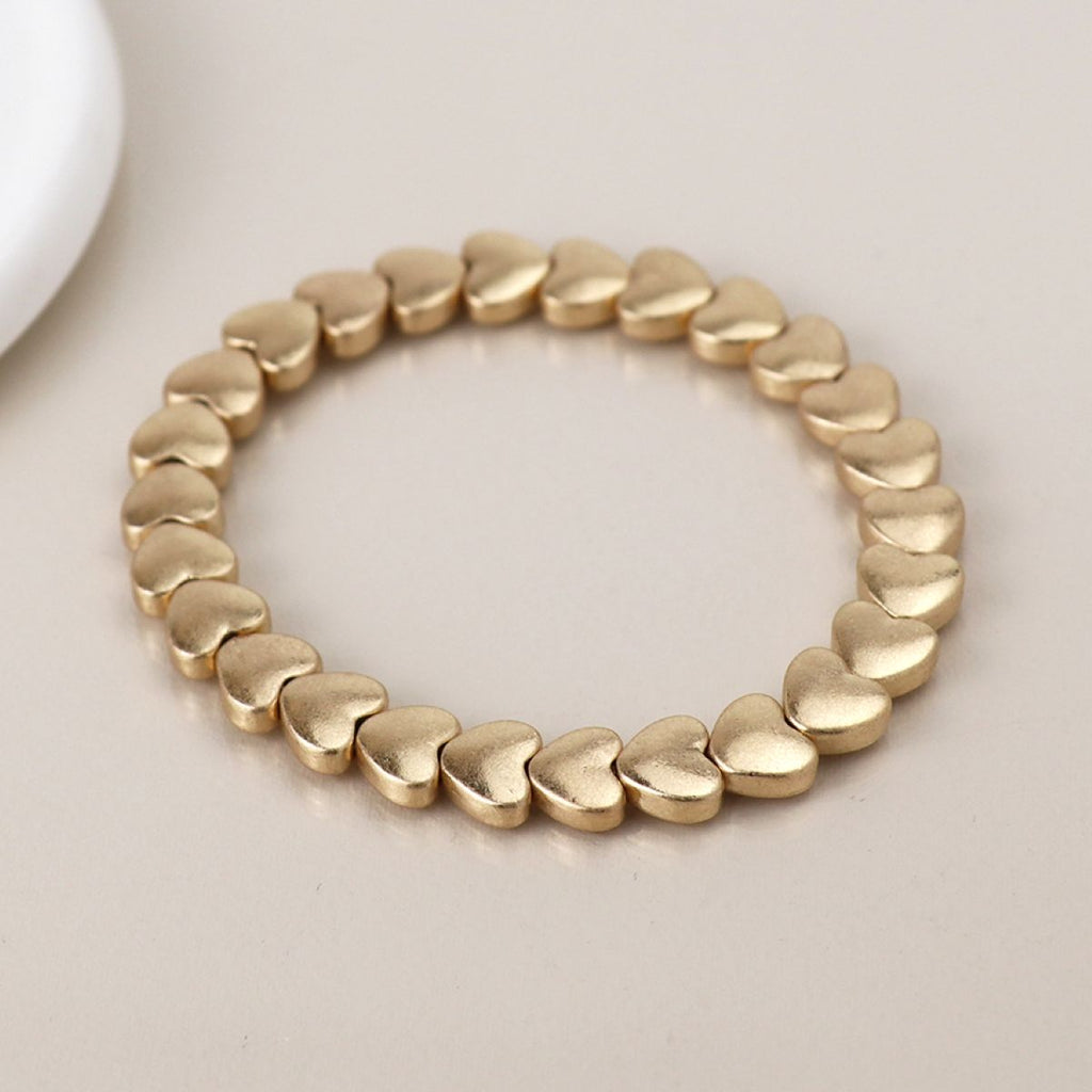 Matt gold bracelet with heart-shaped beads on a light background