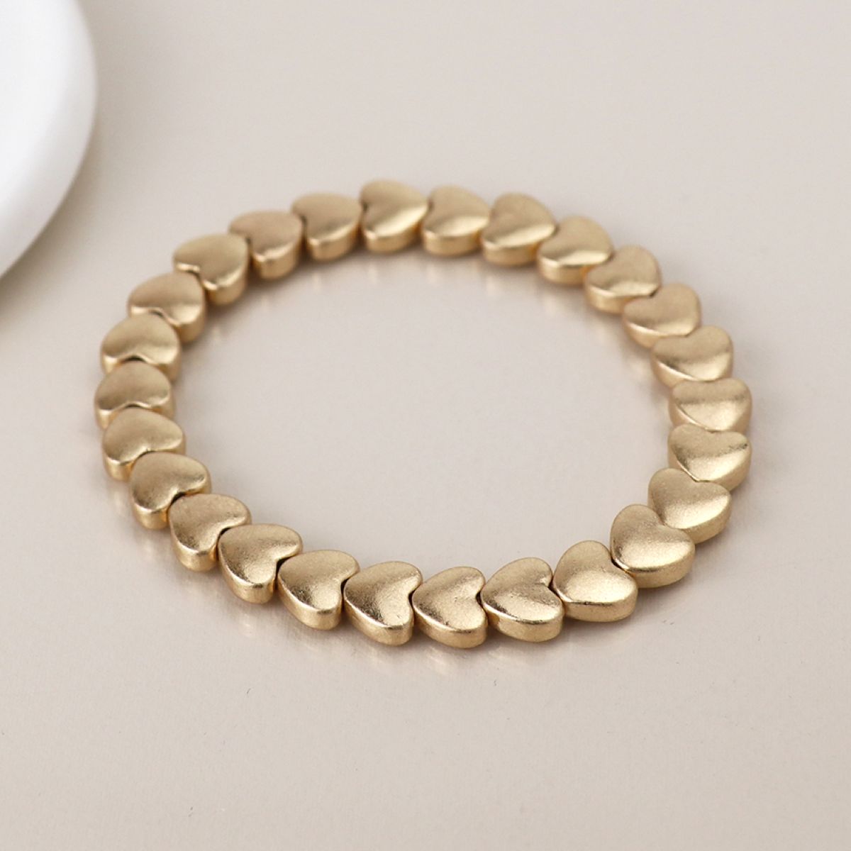 Matt gold bracelet with heart-shaped beads on a light background