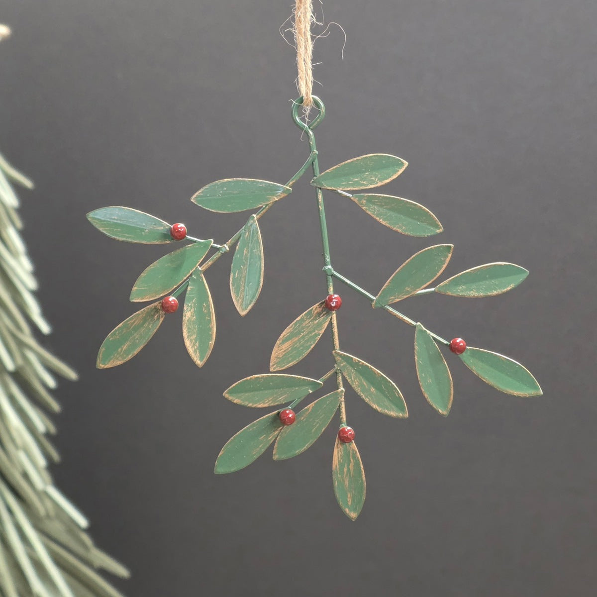 A metal hanging decorative branch ornament with multiple green leaves and small red berries on a dark grey background.