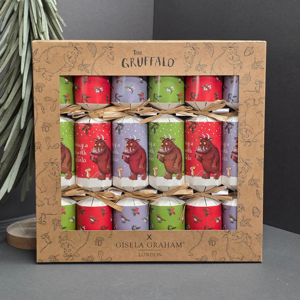 A boxed set of Gruffalo-themed party crackers from Gisela Graham London, displayed in a brown cardboard gift box with printed illustrations. The crackers are wrapped in red, green, and lavender paper featuring the Gruffalo character and festive designs, tied with thin twine.