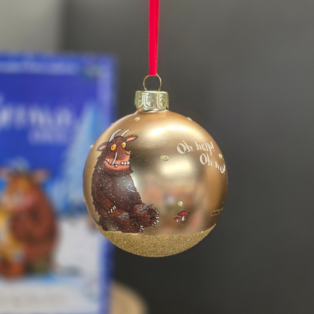 A hand-painted gold Christmas bauble ornament featuring the Gruffalo with a red hanging ribbon, shown against a blurred background.