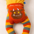 A close-up of a children's outfit featuring a bright orange waistband with embroidered text reading 'The Gruffalo x Blade & Rose' and a large brown monster face motif, paired with striped legs in orange, yellow, and gray-green on a white background.