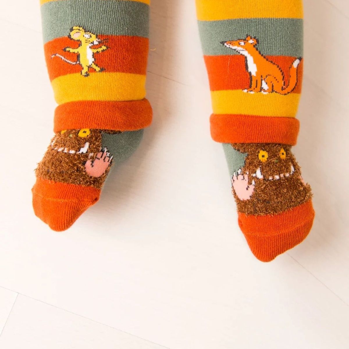 A pair of children's striped socks with cartoon animal and monster designs, shown on a child's feet against a light background.
