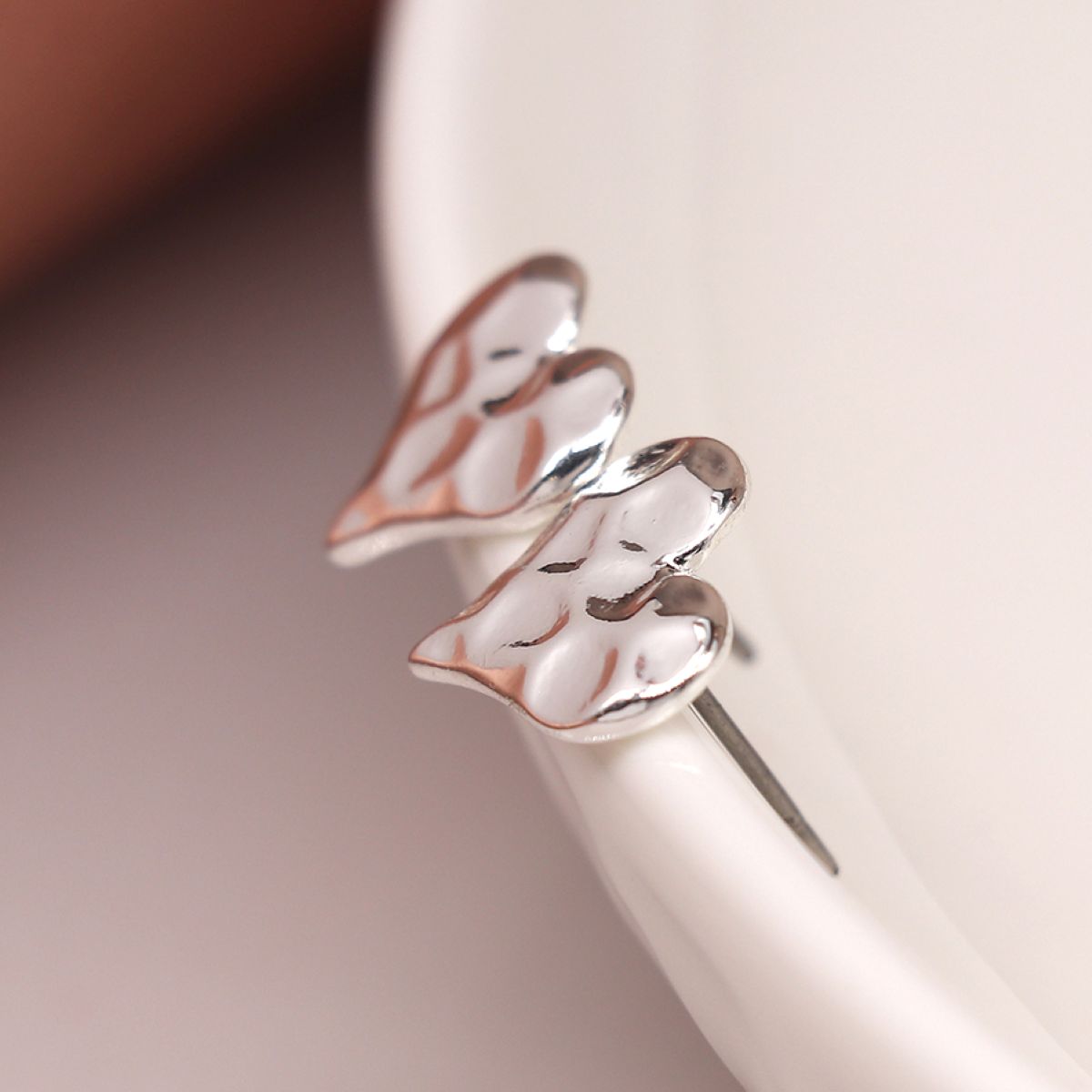Silver hammered heart-shaped earrings on a ceramic dish display