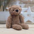 A brown soft fuzzy plush teddy bear toy, with black eyes and nose, on a wooden surface with a blurred star-shaped object in the background
