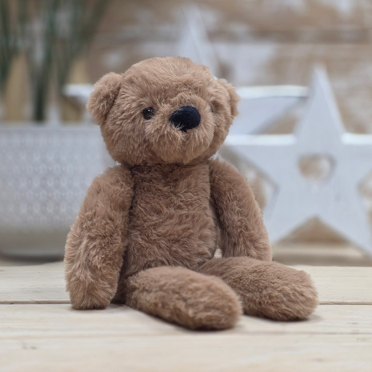 A brown soft fuzzy plush teddy bear toy, with black eyes and nose, on a wooden surface with a blurred star-shaped object in the background
