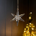 Decorative glass star-shaped ornament hanging against a blurred Christmas tree background.