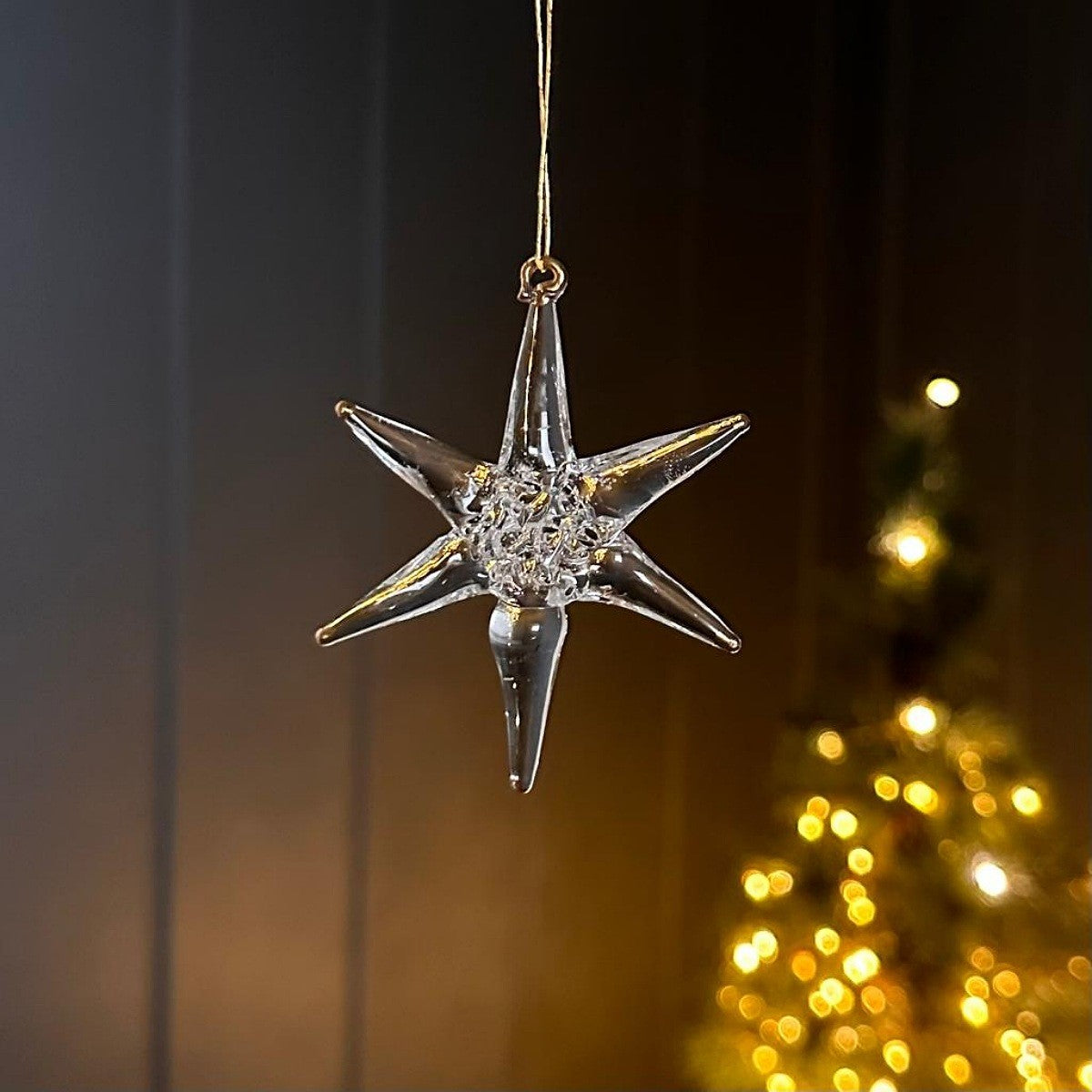 Decorative glass star-shaped ornament hanging against a blurred Christmas tree background.