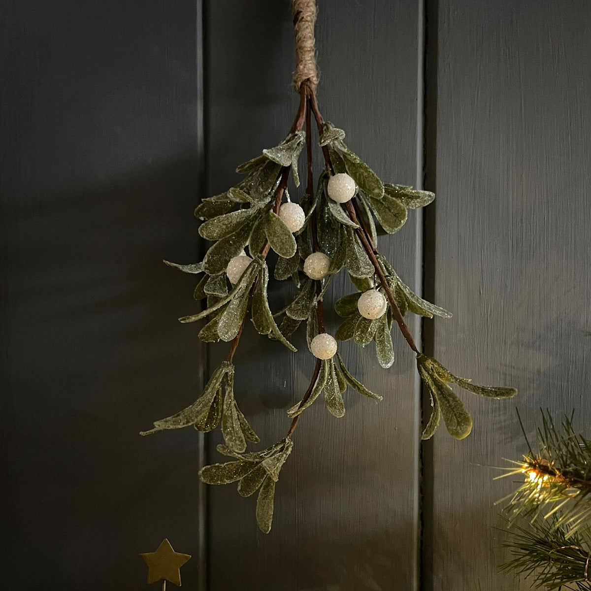 Decorative sparkly mistletoe hanging against a dark wooden background