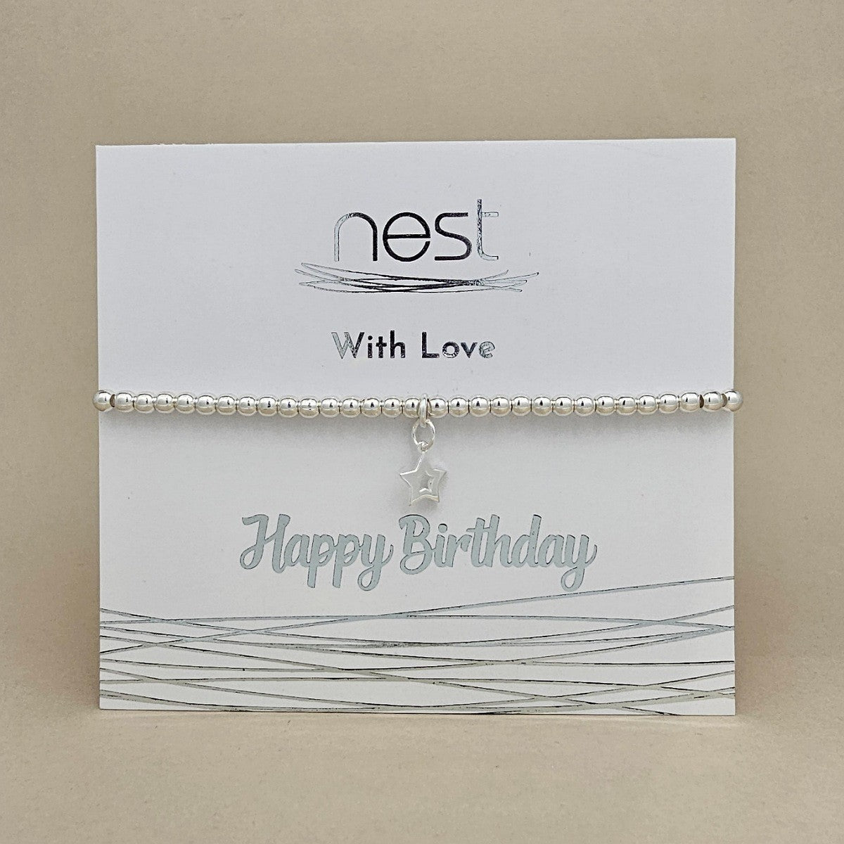 A silver beaded bracelet with a dangling star charm, presented on a white 'nest' brand birthday card that reads 'With Love' and 'Happy Birthday', set against a neutral beige background.