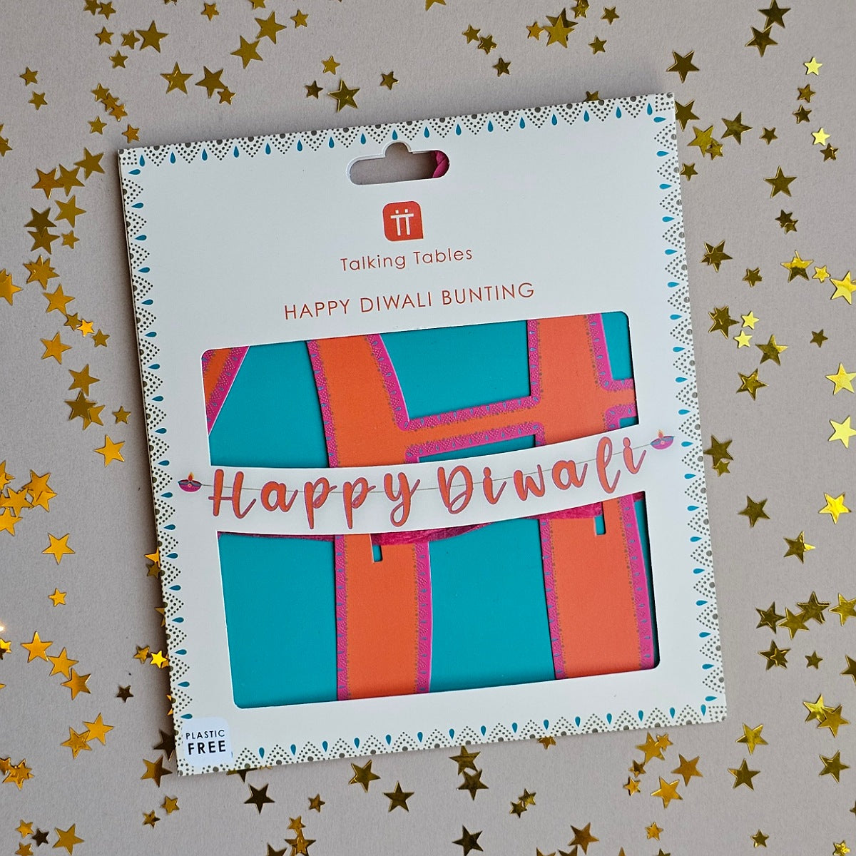 Happy Diwali Bunting in its retail packaging, displayed on a gray background scattered with gold star confetti. The packaging is white with a decorative border and a clear window showing the colorful bunting inside.