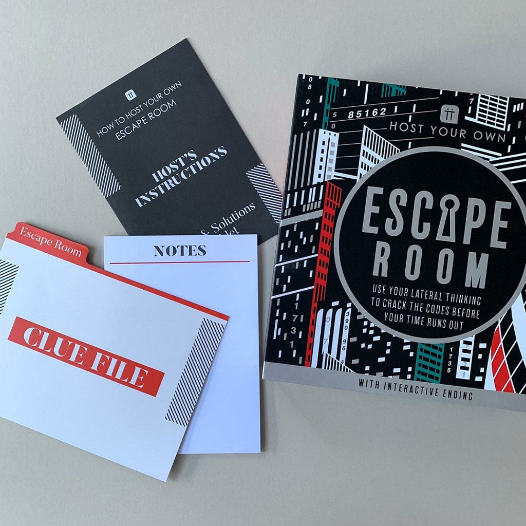 Escape Room kit contents arranged on a light gray surface, including a black instruction booklet, a white notes card, a white clue file with red accents, and a black-and-white Escape Room box with red and teal graphic accents.