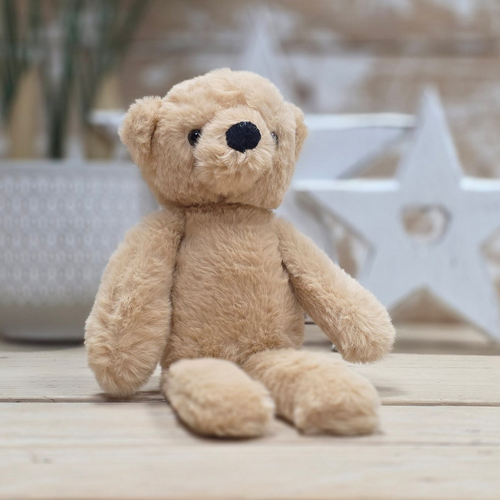 A light brown soft fuzzy plush teddy bear toy, with black eyes and nose, on a wooden surface with a blurred star-shaped object in the background
