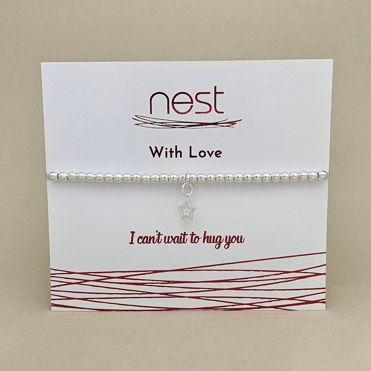 A beaded bracelet with a small silver star charm, displayed on a white card from the brand 'nest' with red text that reads 'With Love' and 'I can't wait to hug you'.