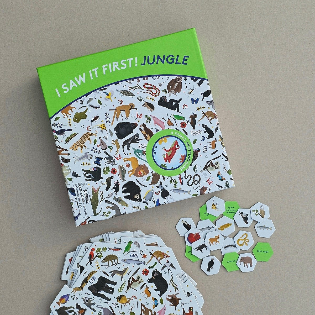 An educational children's game titled 'I SAW IT FIRST! JUNGLE' shown on a neutral grey background, alongside a stack of illustrated jungle-themed tabs and small green hexagonal cards.
