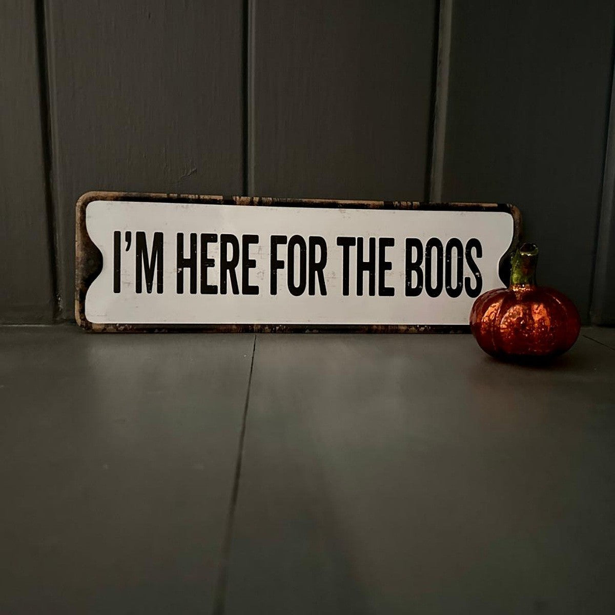 Halloween-themed sign with 'I'm here for the boos' text next to a small pumpkin on a dark surface.