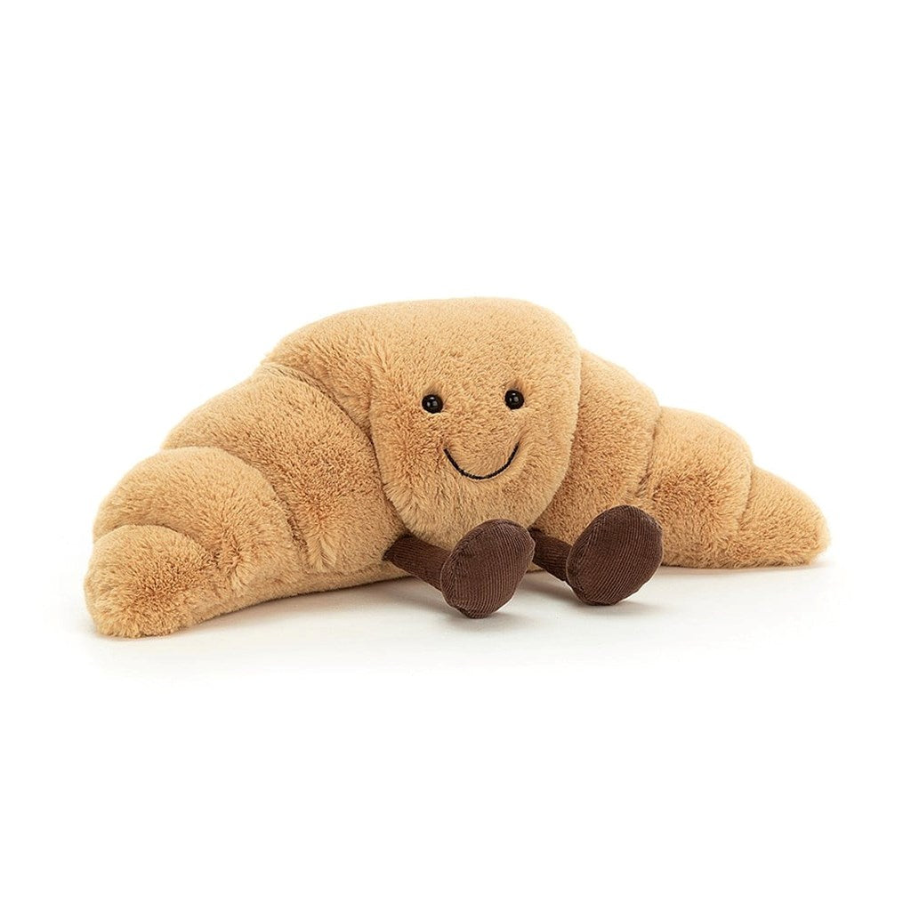 Plush toy shaped like a croissant light brown, brown legs with a smiling face on a white background