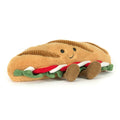 Plush toy shaped like a baguette containing cheese, tomato and lettuce with a smiling face and brown legs on a white background