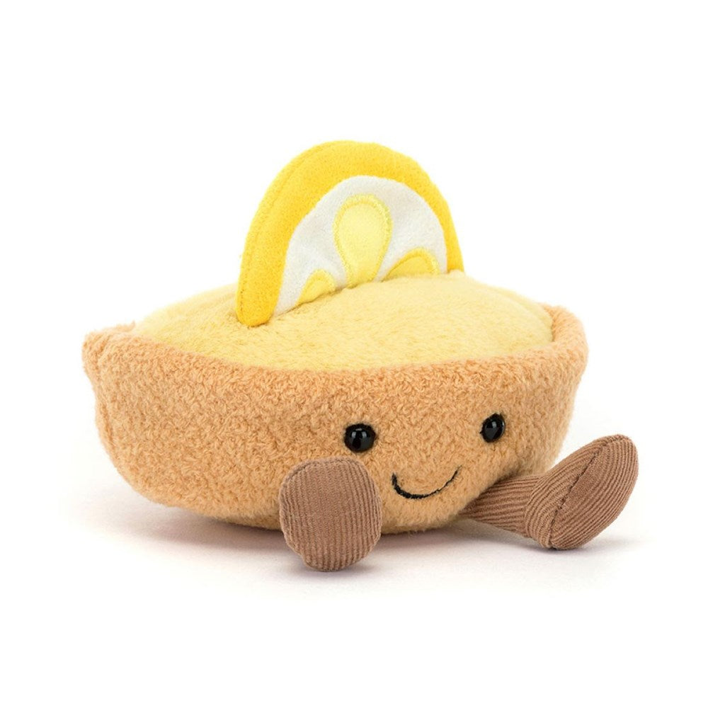 Plush toy resembling a yellow torte au citron with a half lemon piece on top, brown legs with a smiling face on a white background