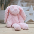 A soft pink plush bunny toy sitting on a light wooden surface with a softly blurred indoor background.
