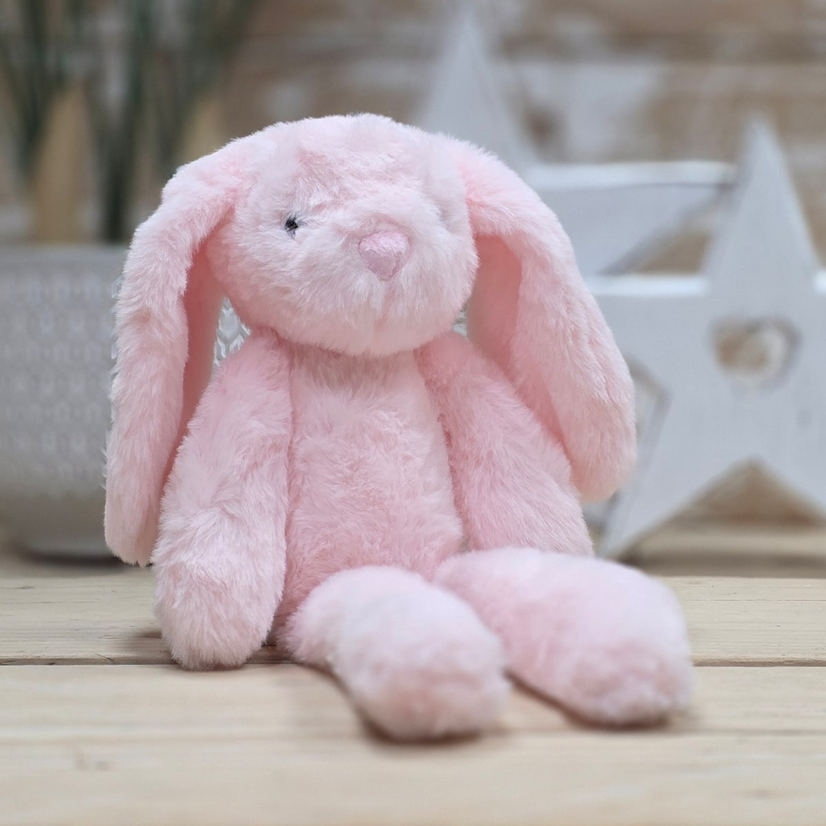 A soft pink plush bunny toy sitting on a light wooden surface with a softly blurred indoor background.
