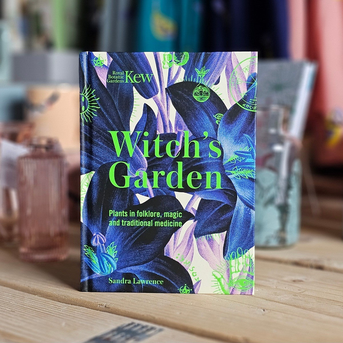 Book titled 'Witch's Garden' by Sandra Lawrence on a wooden surface with a blurred background.
