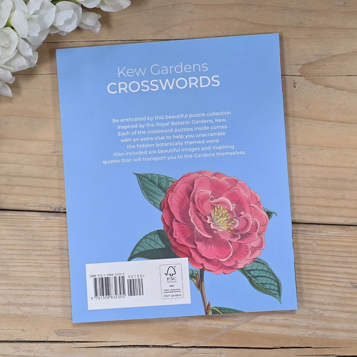 Book titled 'Kew Gardens Crosswords' with a pink flower illustration on a wooden surface. 
