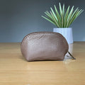 Brown leather purse on a wooden surface with a plant in the background