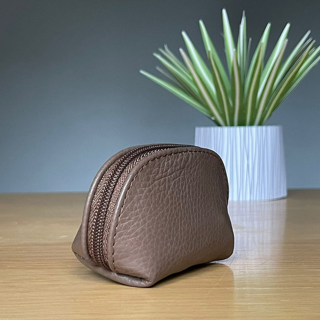 Brown leather zippered purse on a wooden surface with a plant in the background