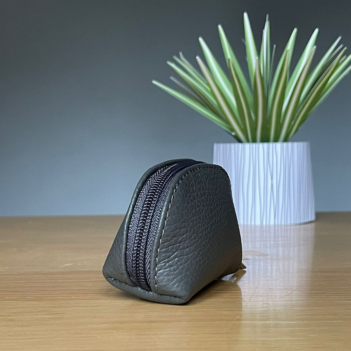 Charcoal grey leather purse with zipper on a wooden surface with a plant in the background