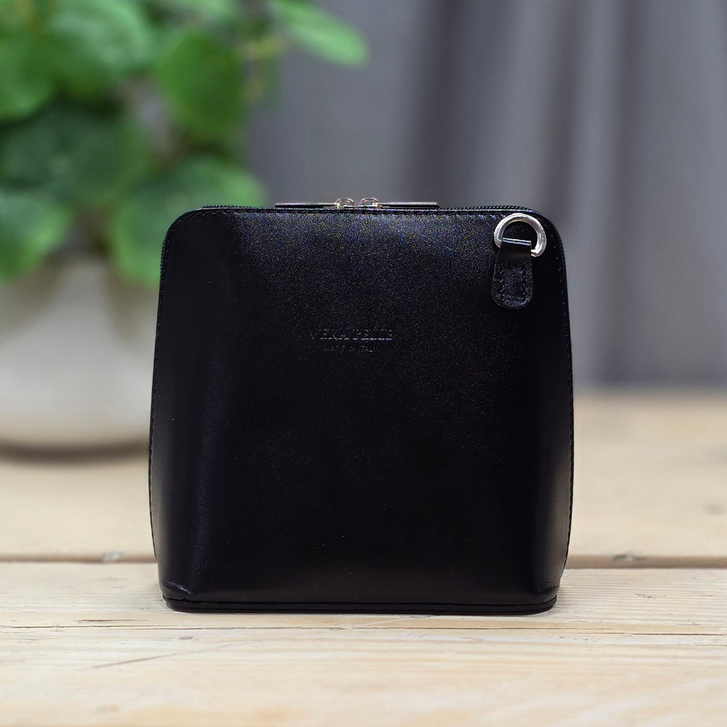 Black leather handbag on a wooden surface with a blurred green plant in the background