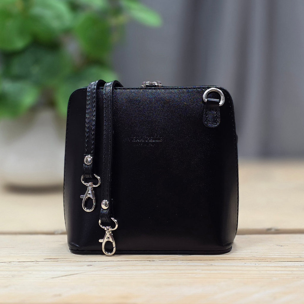 Black handbag with a strap on a wooden surface with a blurred green plant in the background