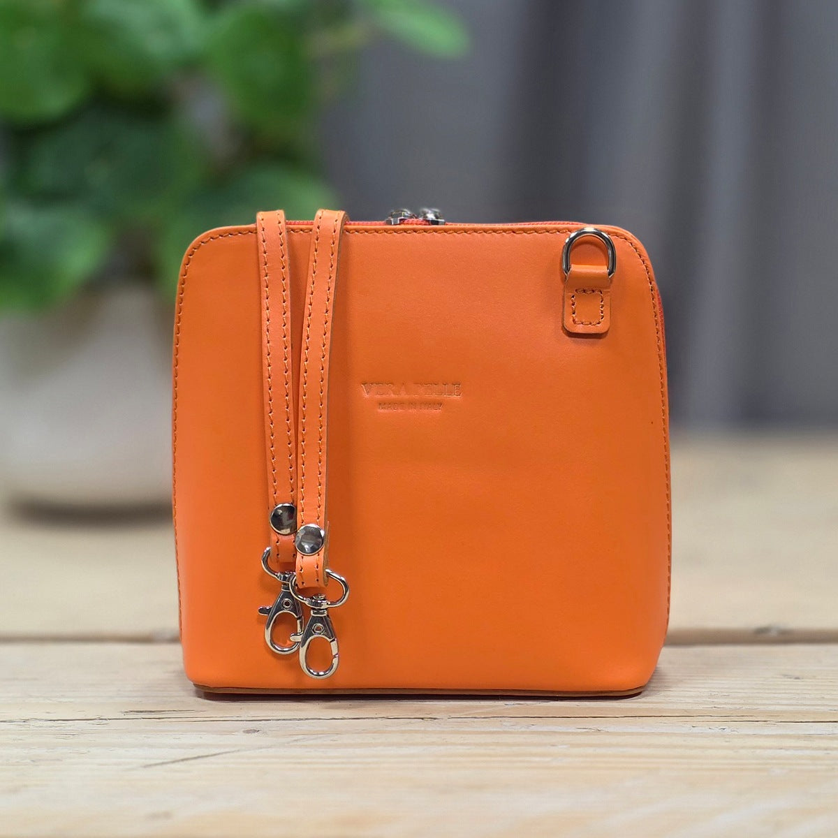 Orange leather crossbody bag with a plant in the background