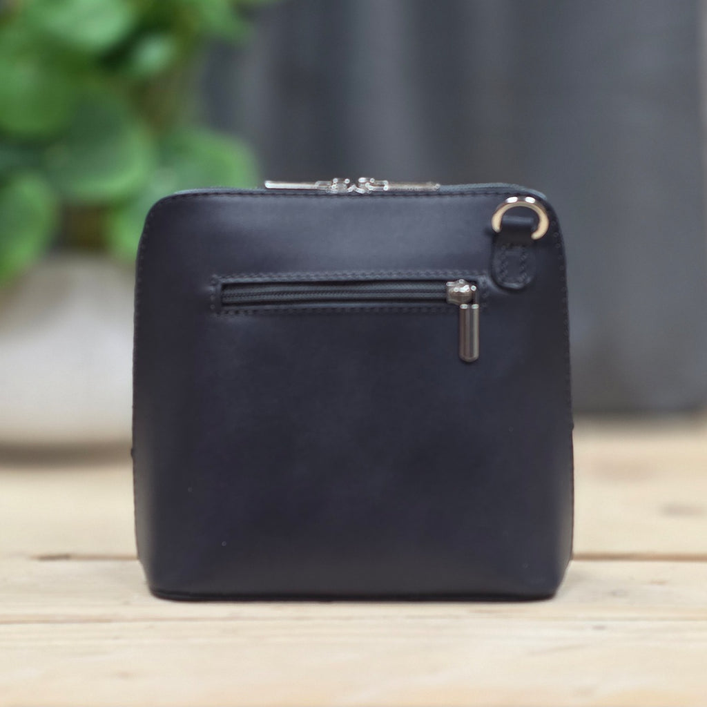 Dark grey leather handbag with a zipper on a wooden surface with a blurred background