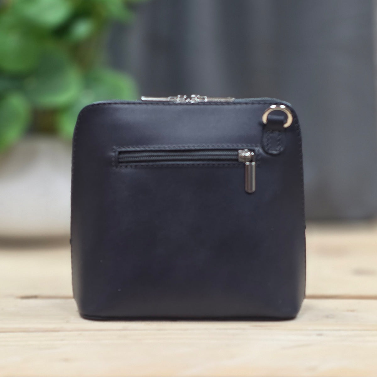 Dark grey leather handbag with a zipper on a wooden surface with a blurred background