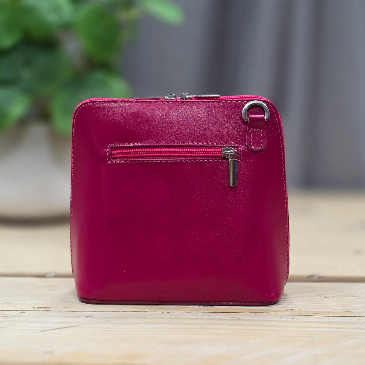 Pink leather handbag with a zipper on a wooden surface with a blurred green plant in the background