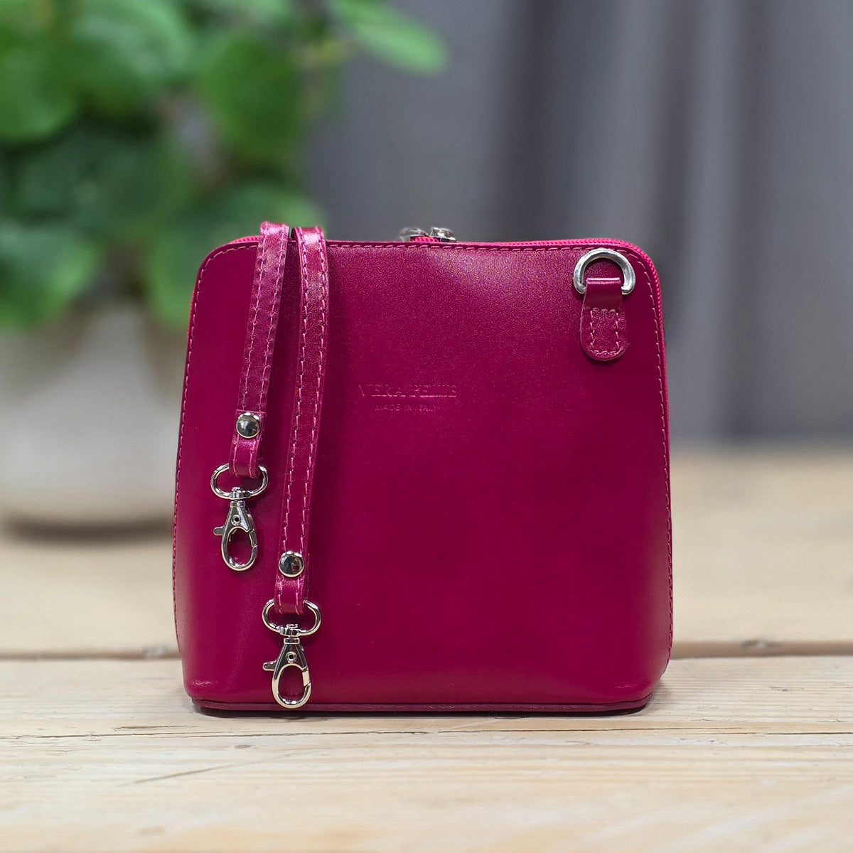 Pink handbag with silver hardware on a wooden surface with a blurred green plant in the background