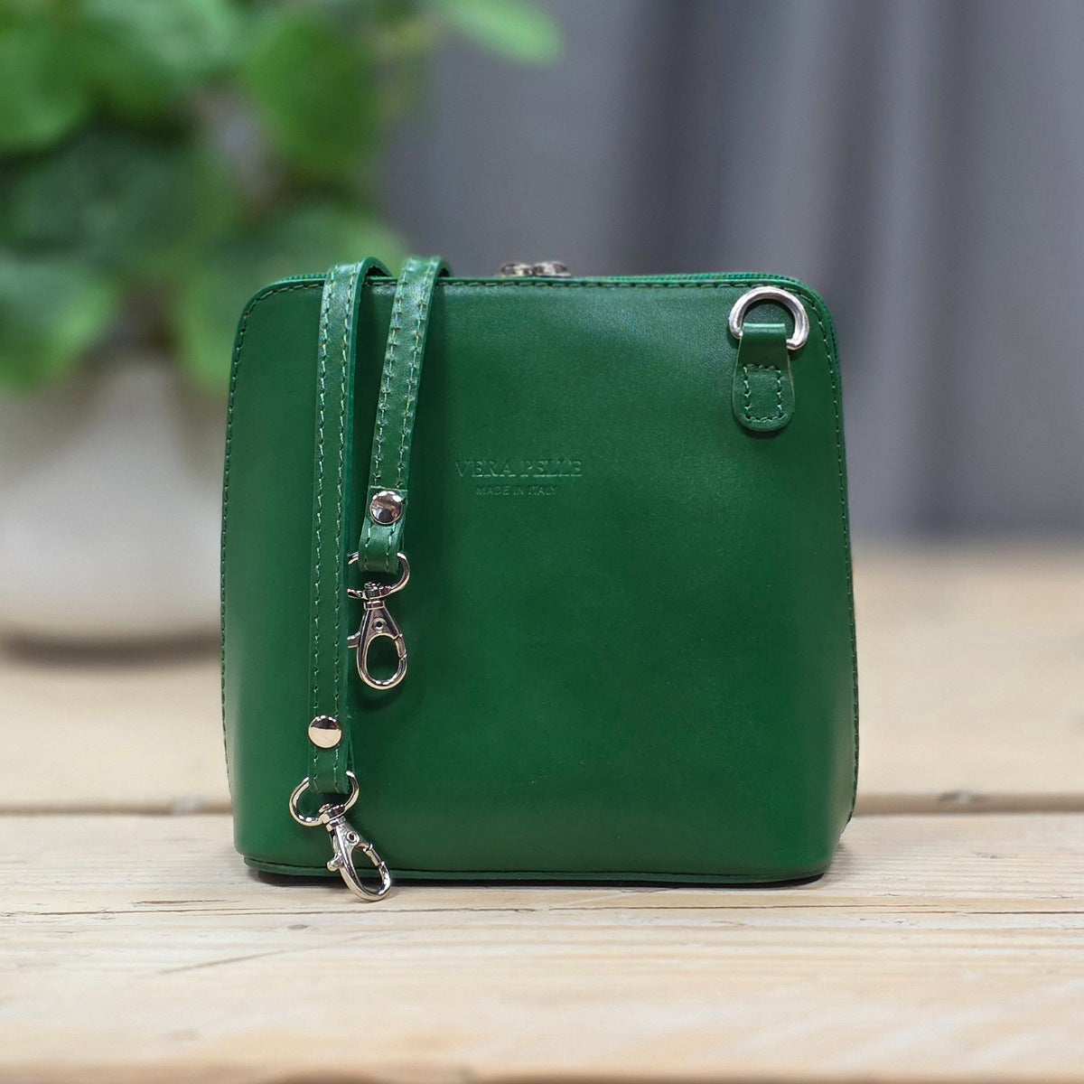 Green leather handbag with a strap on a wooden surface with a blurred background