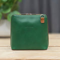 Green leather handbag with brown zipper pull on a wooden surface