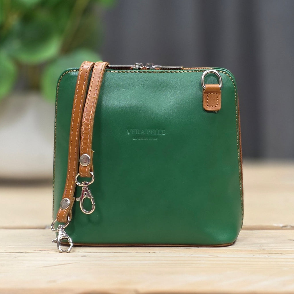 Green handbag with brown strap on a wooden surface