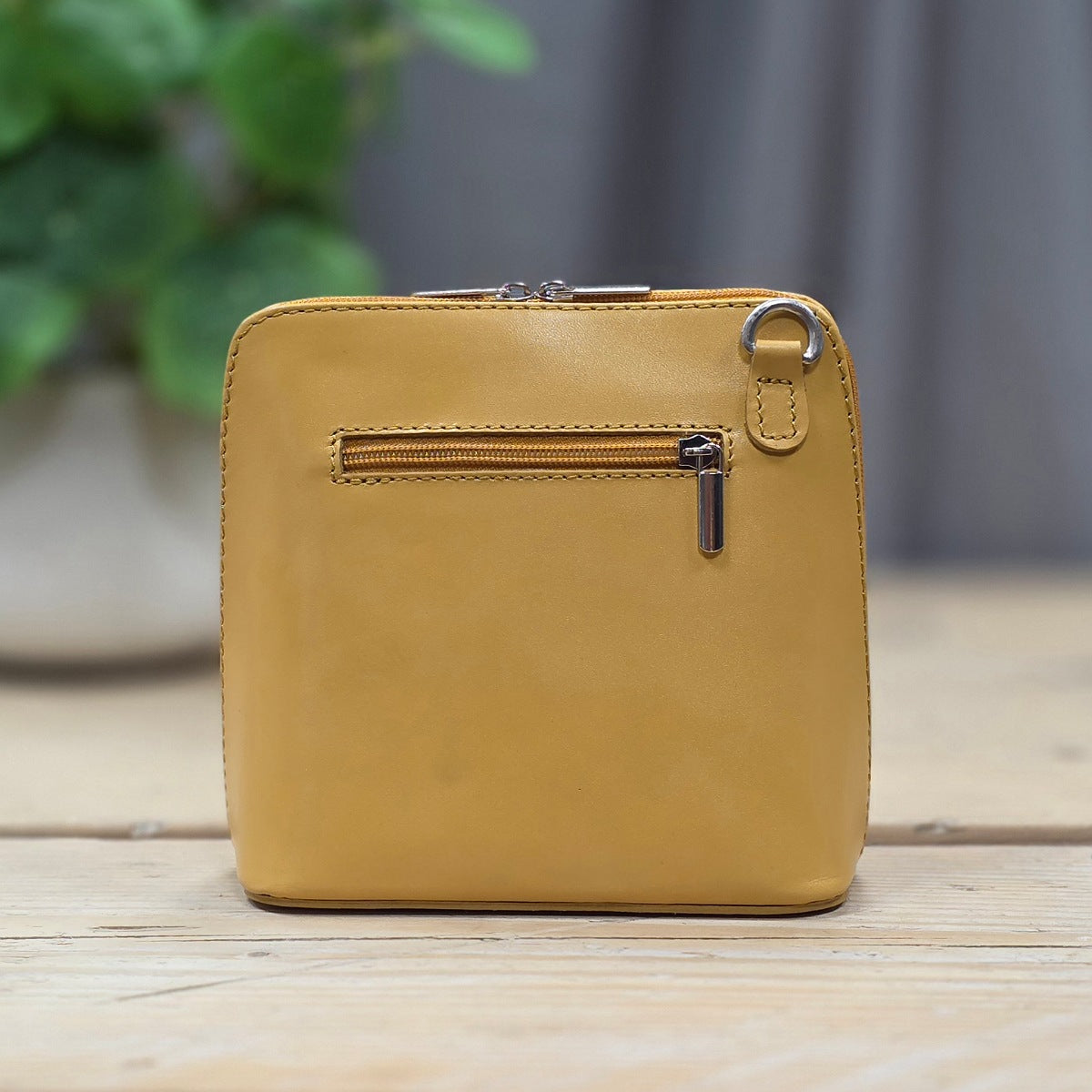 Yellow leather handbag with a zipper on a wooden surface with a blurred green plant in the background