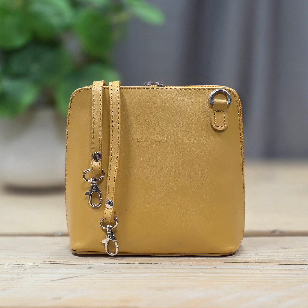 Yellow leather crossbody bag on a wooden surface with a blurred green plant in the background