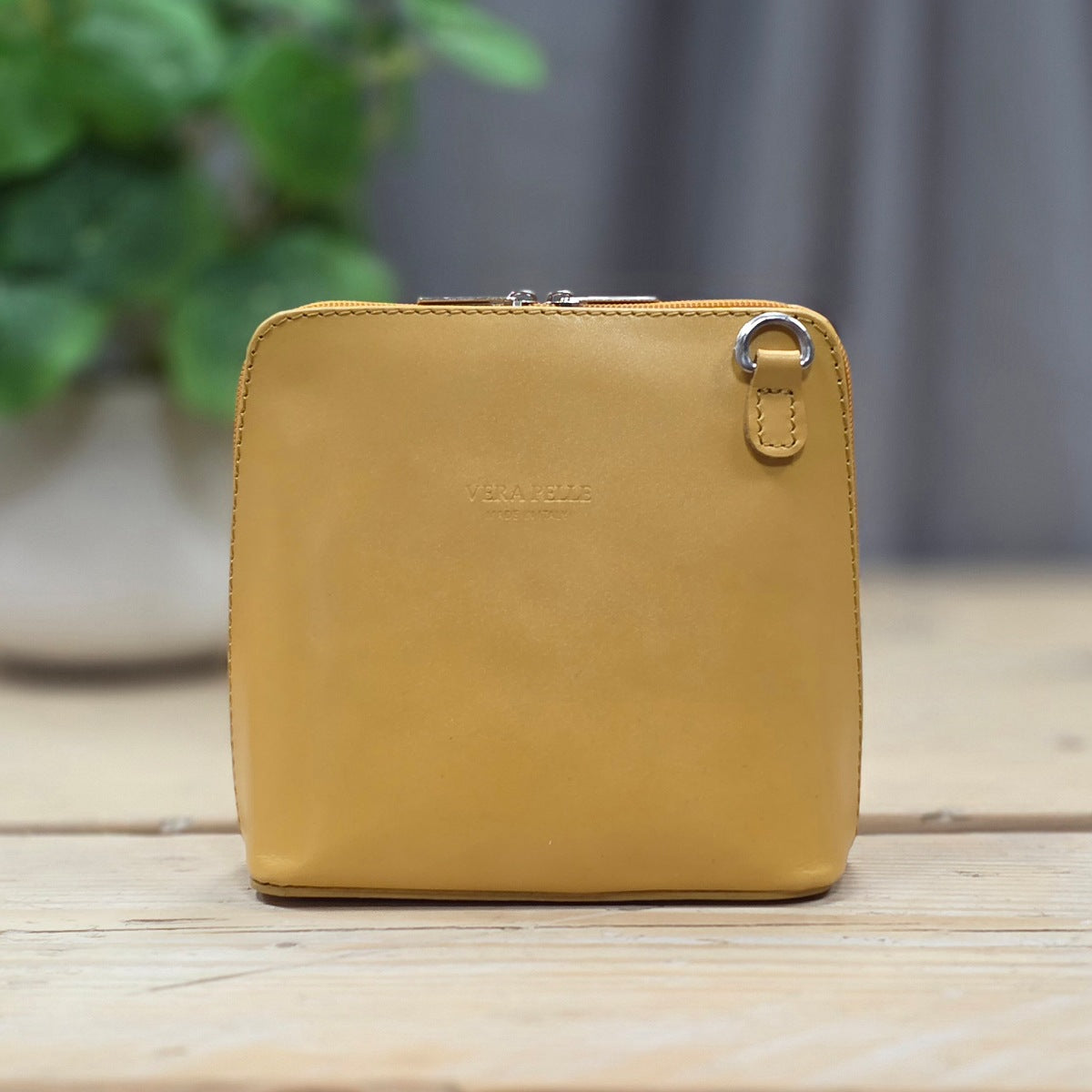 Yellow leather handbag on a wooden surface with a blurred green plant in the background