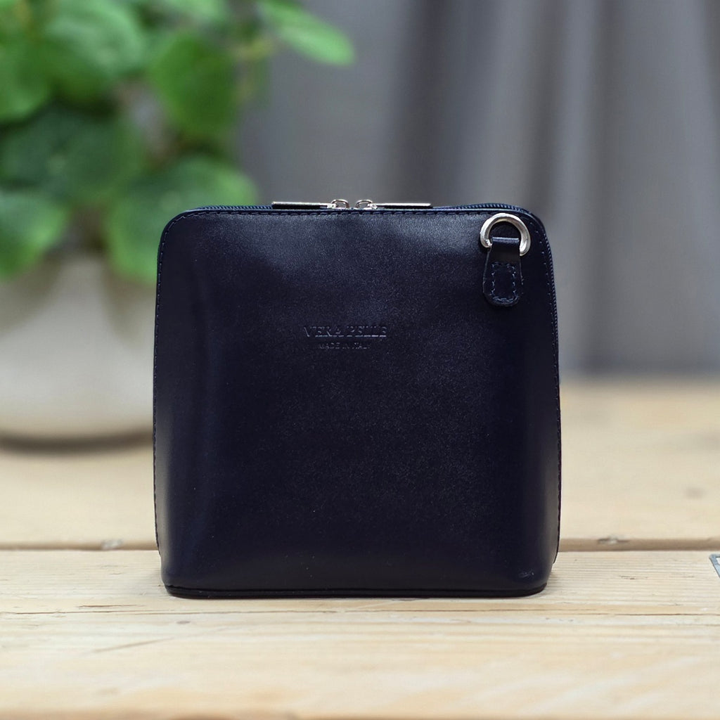 Navy blue leather handbag on a wooden surface with a blurred green plant in the background