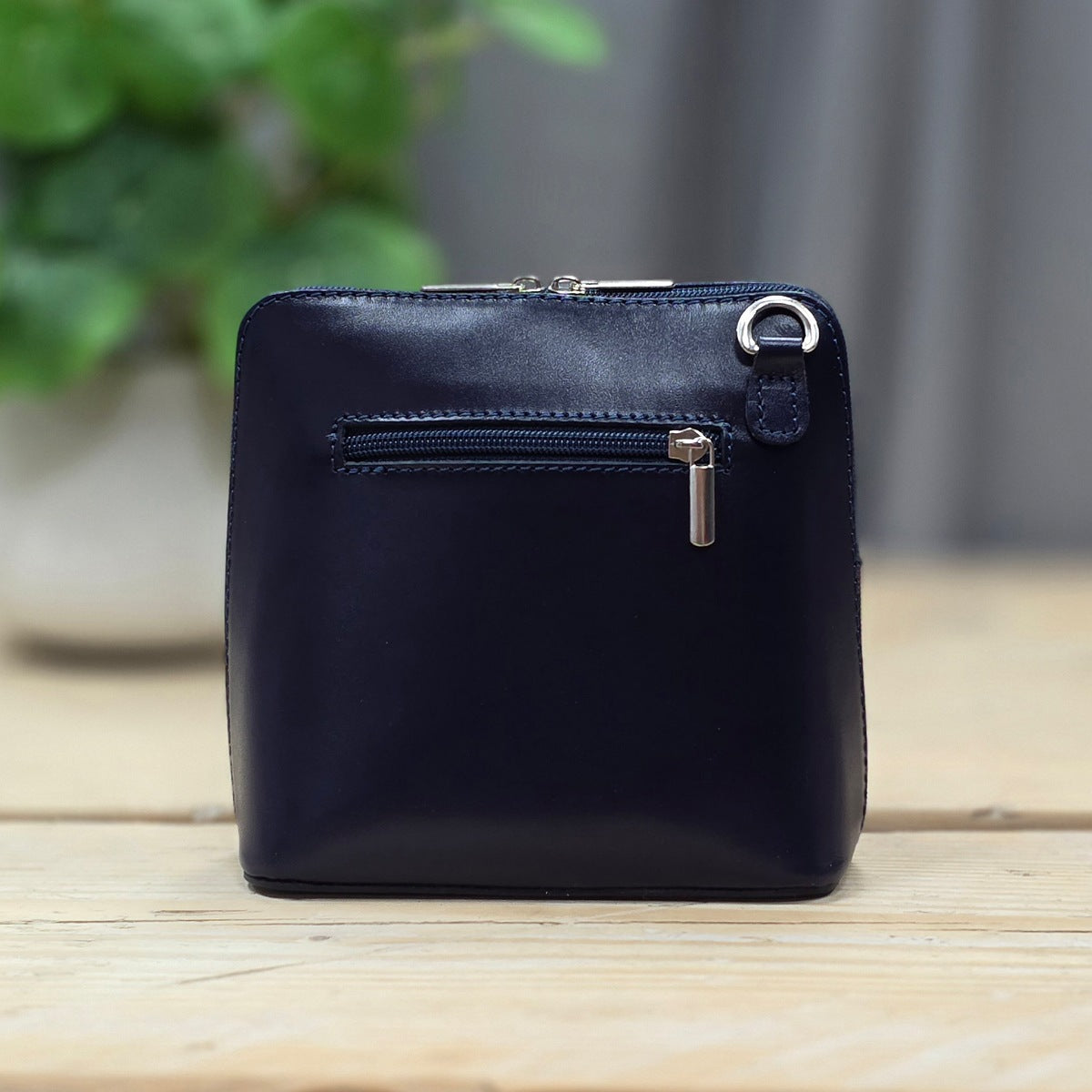 Navy blue leather handbag on a wooden surface with a blurred green plant in the background